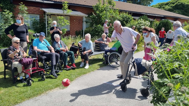 Äldre man kastar bowlingklot i solen. Andra äldre tittar på.