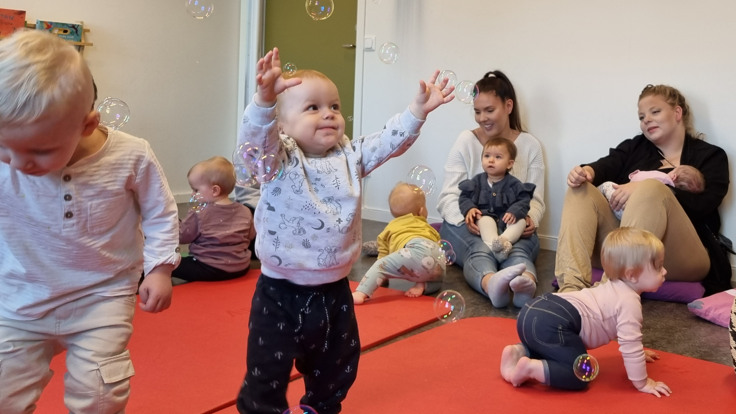 Kvinna blåser såpbubblor. Litet barn försöker fånga bubblorna. 